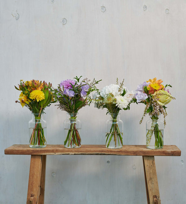 Four small bouquets in jars lined up on wooden stool