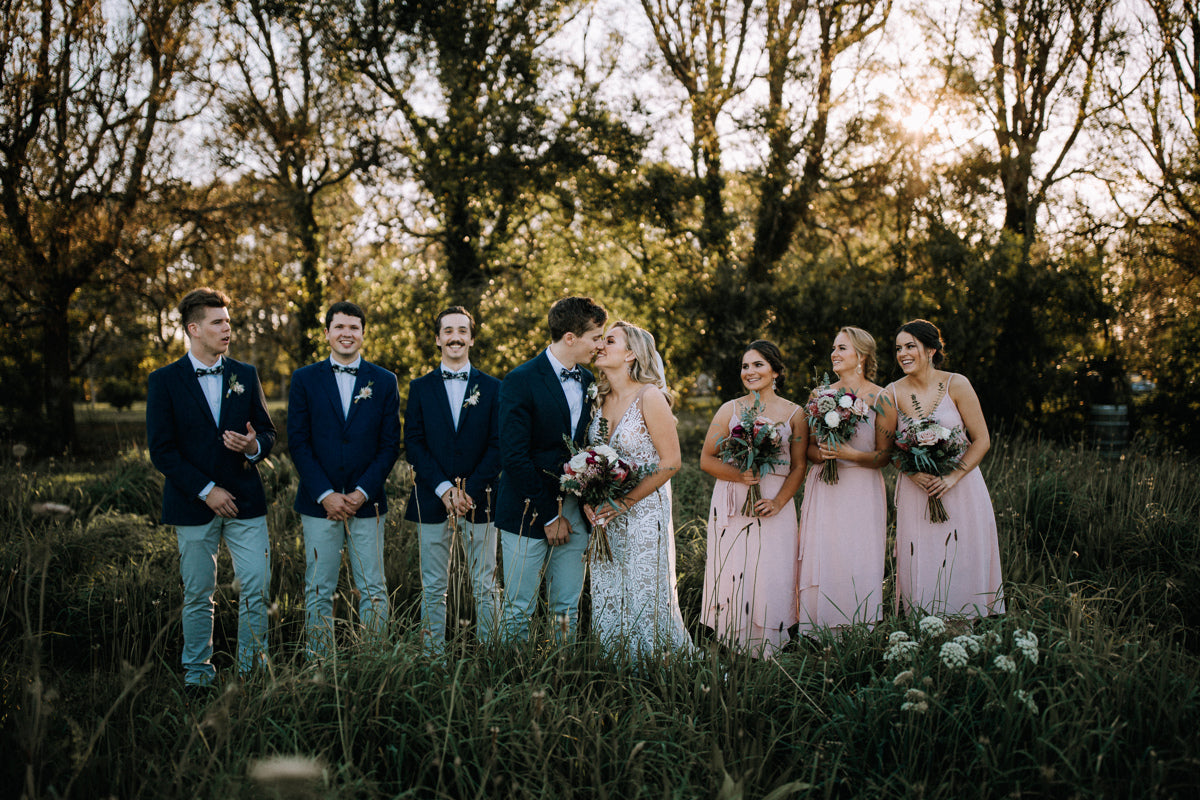 BRIDAL-PARTY-STANDING-IN-FOREST-WHILST-THEY-KISS