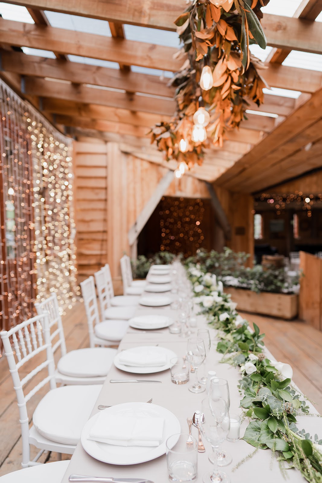BRIDAL_TABLE_AT_WEDDING_INSIDE_BARN_WITH_GREEN_FLORAL_TABLE_SETTING