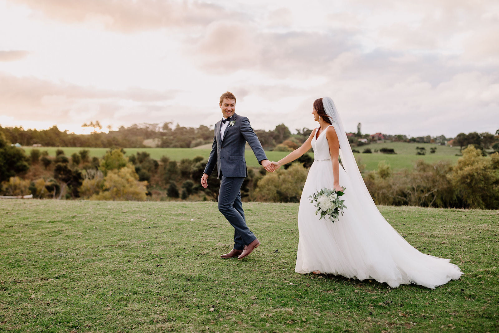 BRIDE-AND-GROOM-WALKING-IN-FIELD-SUNSET