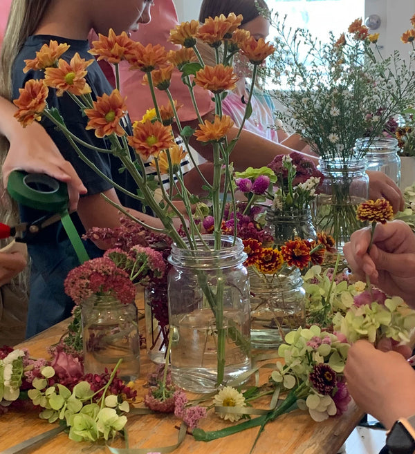 Colourful flowers being arranged in jars on table at flower workshop