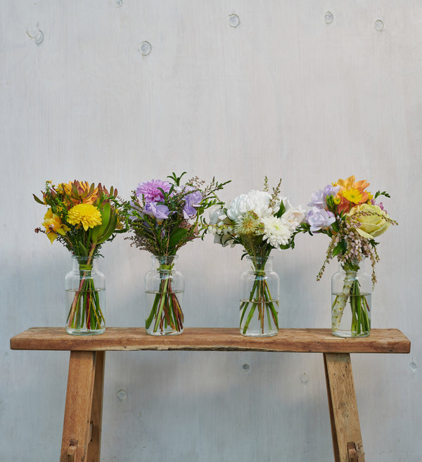 Four-bright-colourful-posy-flower-bouquets-in-glass-jars-on-wooden-stool