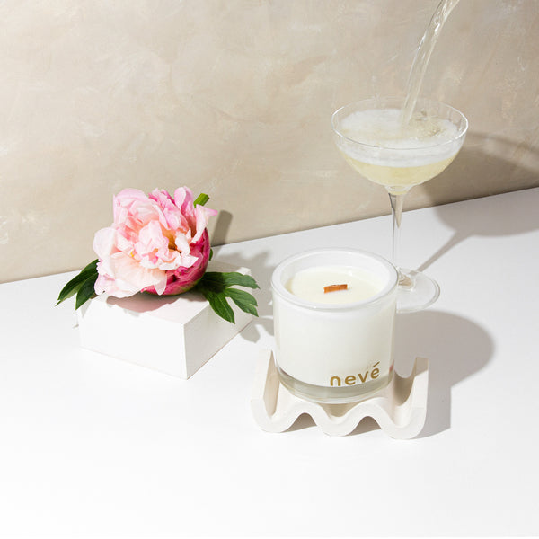White candle with peonies and prosecco being poured into a champagne glass