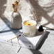 Lit white candle on coffee table book with flower vase