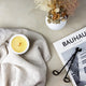 Over-head view of lit white candle on sheet with flower vase and magazine