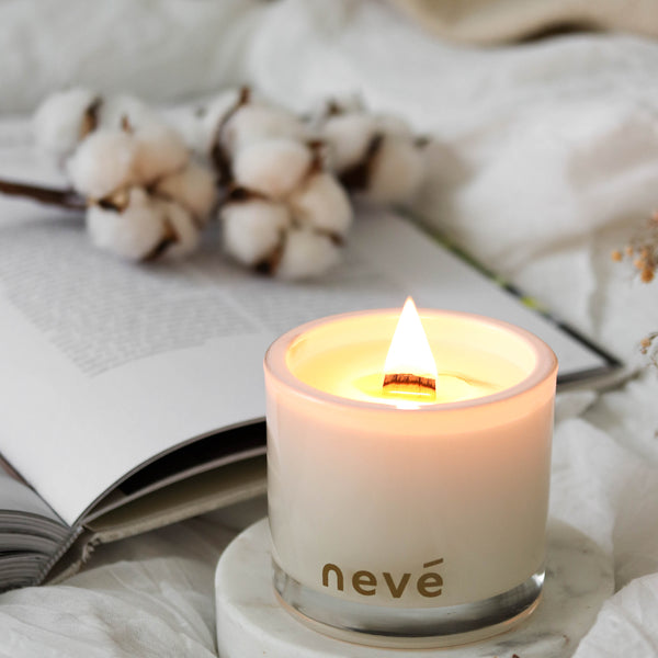 Lit white candle on marble stand on bed with book and cotton stems